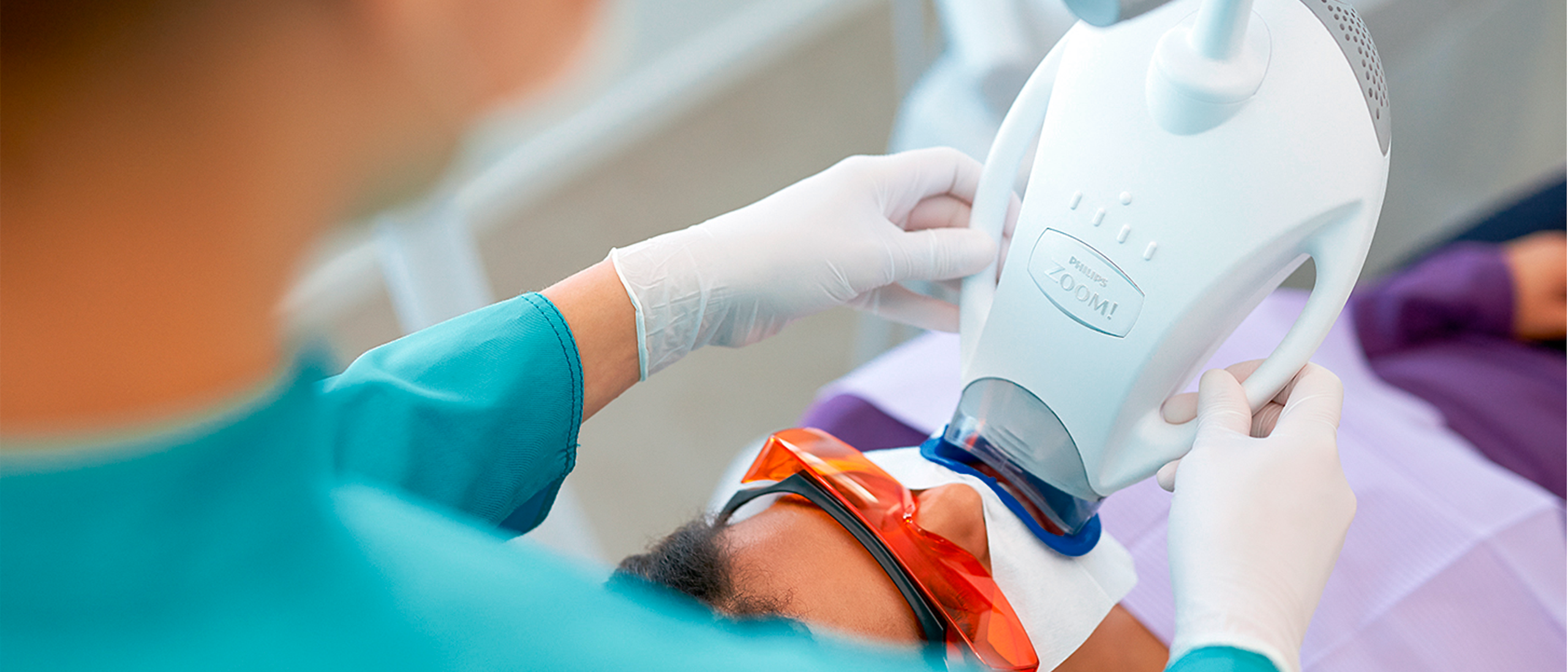 5fd12c34d6f645b7a86db443015713de | No Gaps Dental Dentist performs in-office teeth whitening using a Zoom! light with the patient wearing protective orange eyewear and gloves guiding the device.