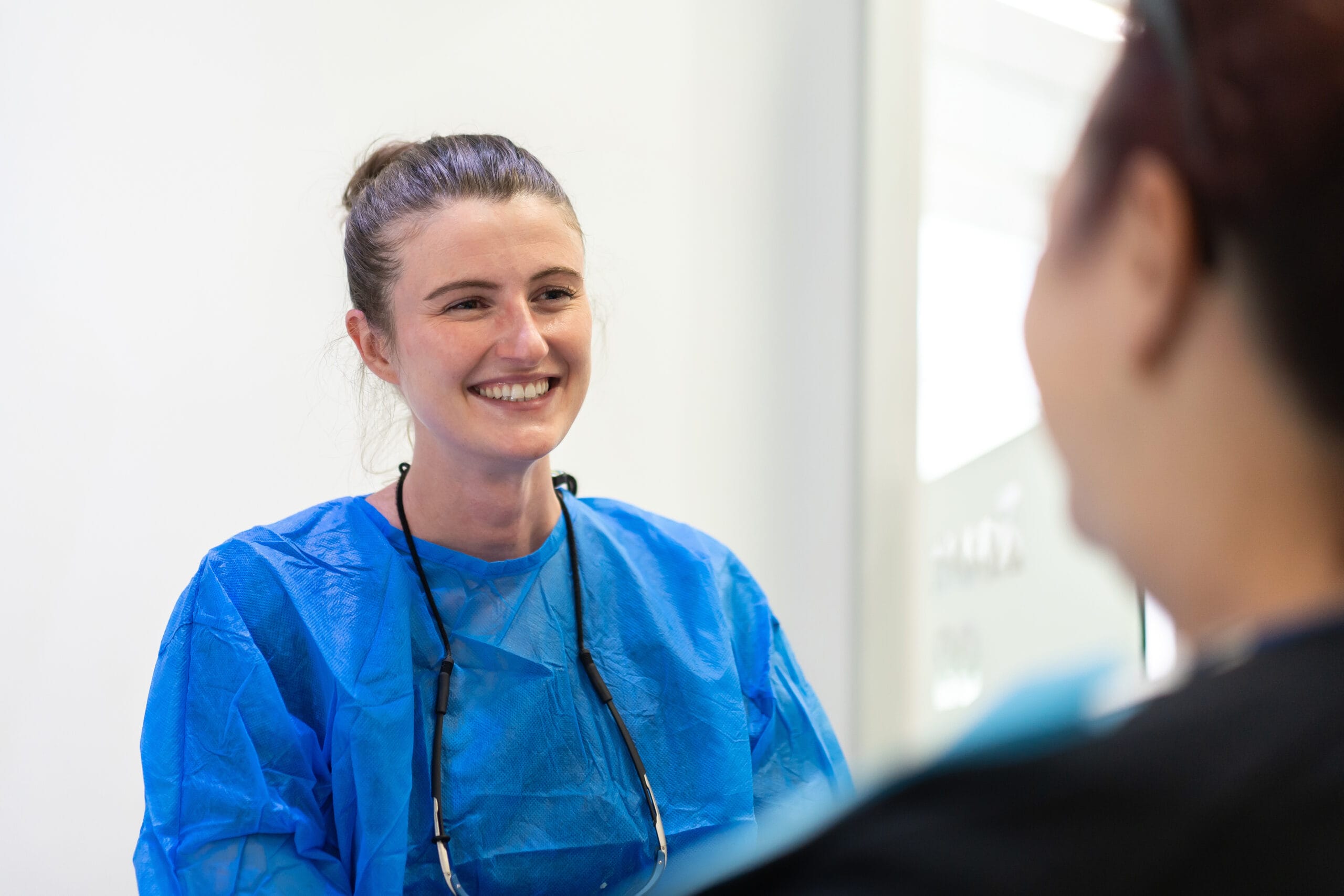 A smiling dental professional in a blue gown interacting with a patient.