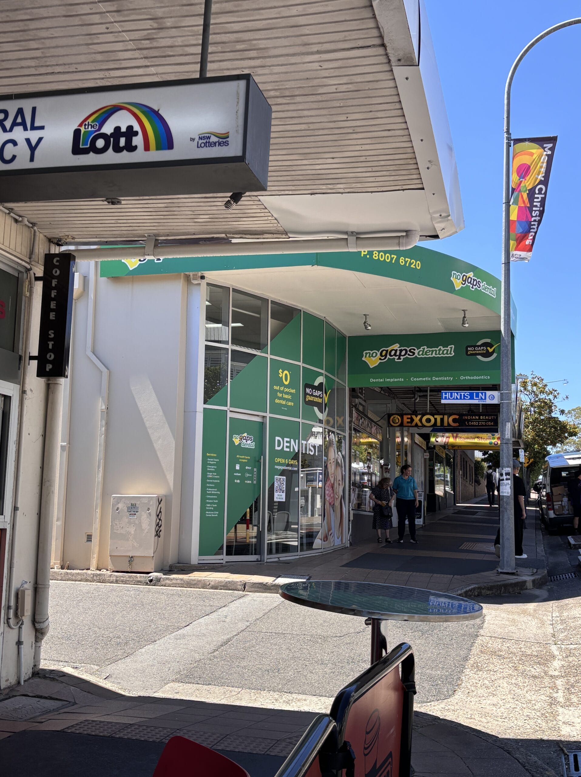 Street view with storefronts including a green 'no gaps dental' sign and a 'Lott' sign on a building awning; pedestrians walking along the sidewalk.