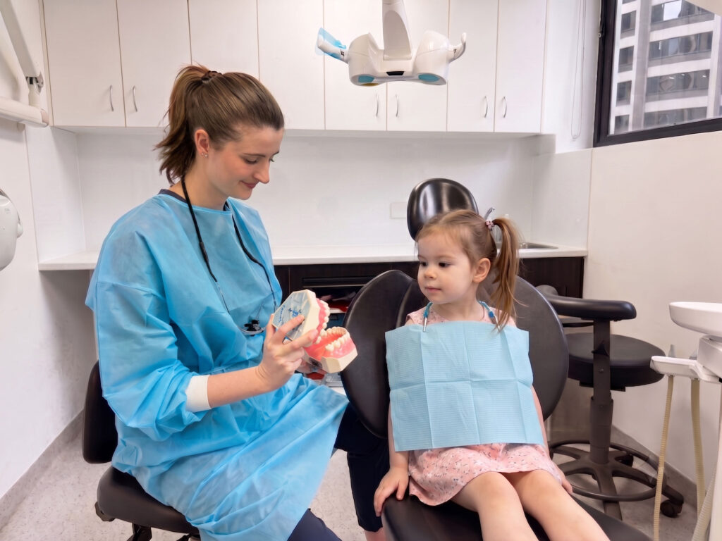 Rebecca-A-Cowie-21_Edited | No Gaps Dental A dental professional shows a plastic teeth model to a young patient.