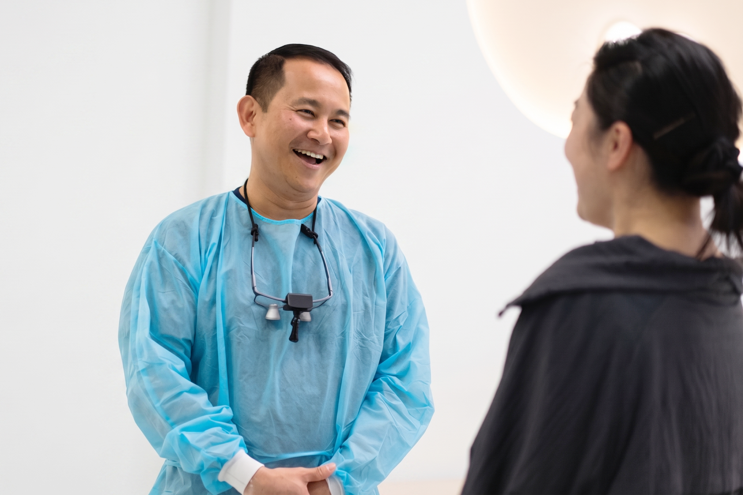 Than-04672_edited | No Gaps Dental Smiling healthcare professional in blue scrubs talking with a patient in a clinic.